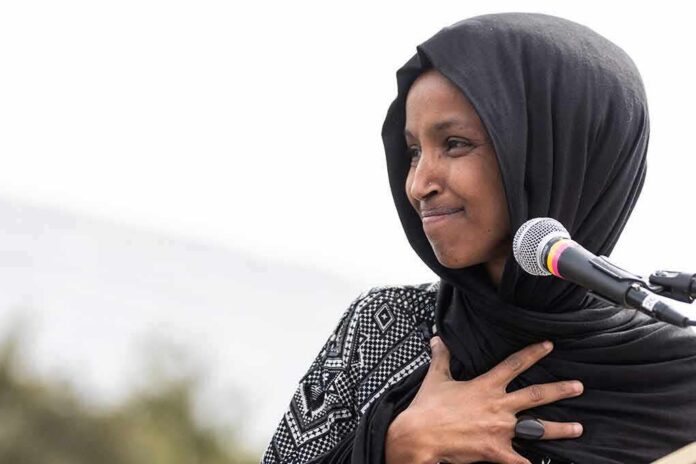 shutterstock_1369296269 Ilhan Omar speaking at a microphone with hand on chest