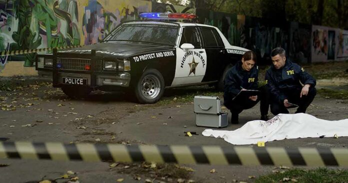 Crime scene with police car and two investigators by a covered body