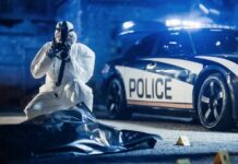 forensic investigator photographing crime scene near police car