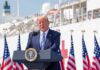 Trump Courts Fetterman – Invites Him To Join Him Donald Trump speaking at a podium with American flags and a ship in the background